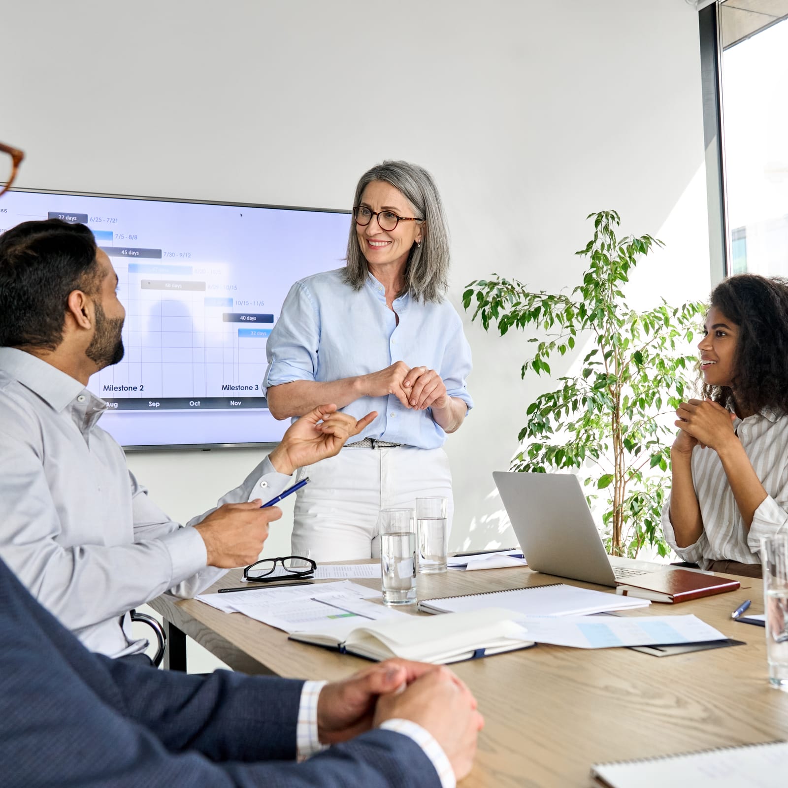 A manager presenting delivery milestones to an engaged team in a bright meeting room